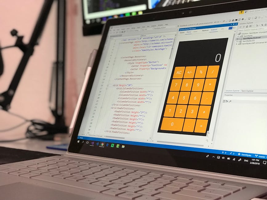 A close-up view of a laptop keyboard and screen situated on a desk or table, displaying lines of code in a text editor alongside a digital calculator interface with orange buttons for numbers and basi